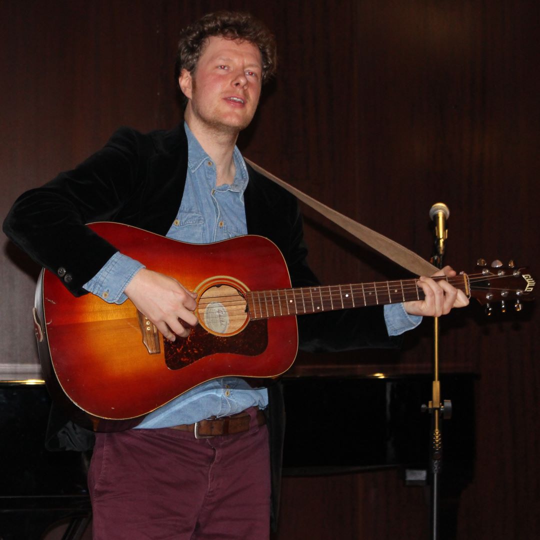 Ein Mann steht auf einer Bühne, spielt eine Gitarre und singt.